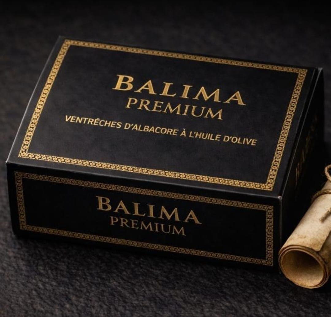 Coffret noir et or Balima Premium, ventrèches à l’huile d’olive, posé près d’un parchemin roulé